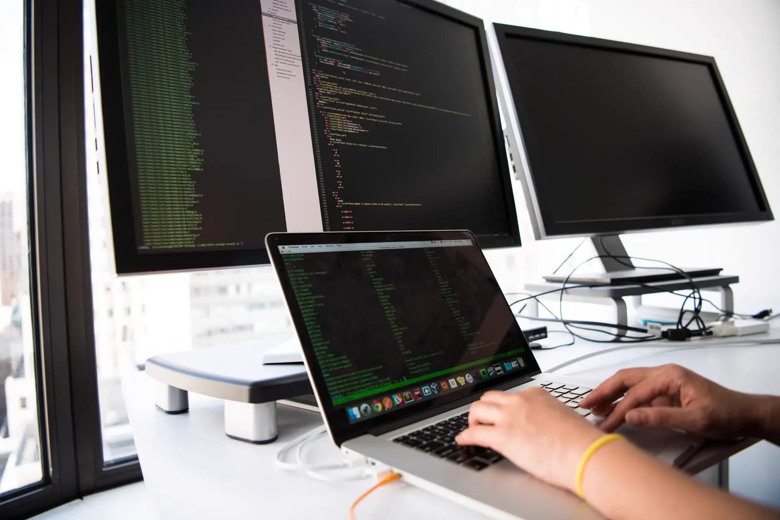 A developer working on a laptop in front of desktop monitors